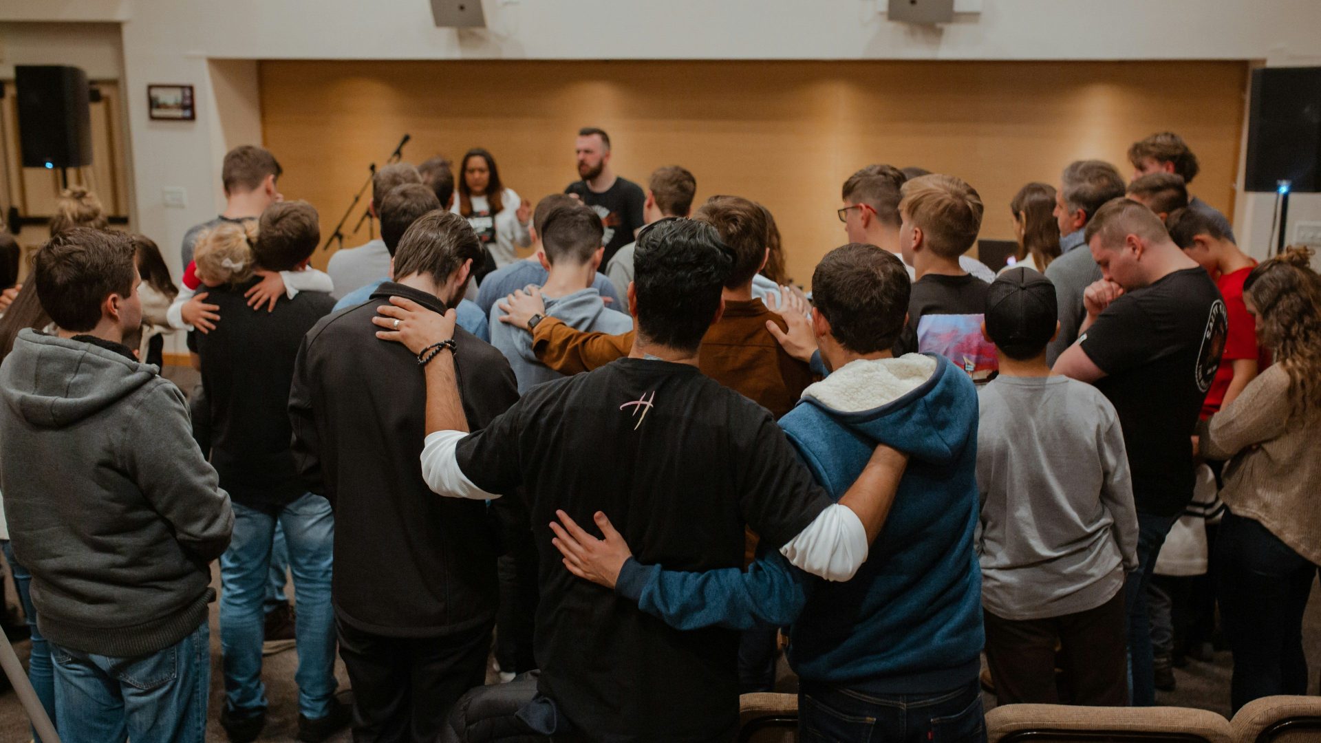 A group of people standing together with arms around each other in a room